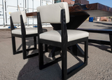 Two blackened chairs with white cushions in an outdoor setting.