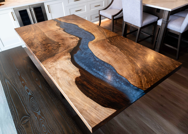 Wooden dining table with a river design inlay, surrounded by chairs and a kitchen area.
Image taken by Haley Knoke