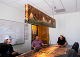 People sitting around a wooden table in an office setting with a decorative light
Image taken by Haley Knoke